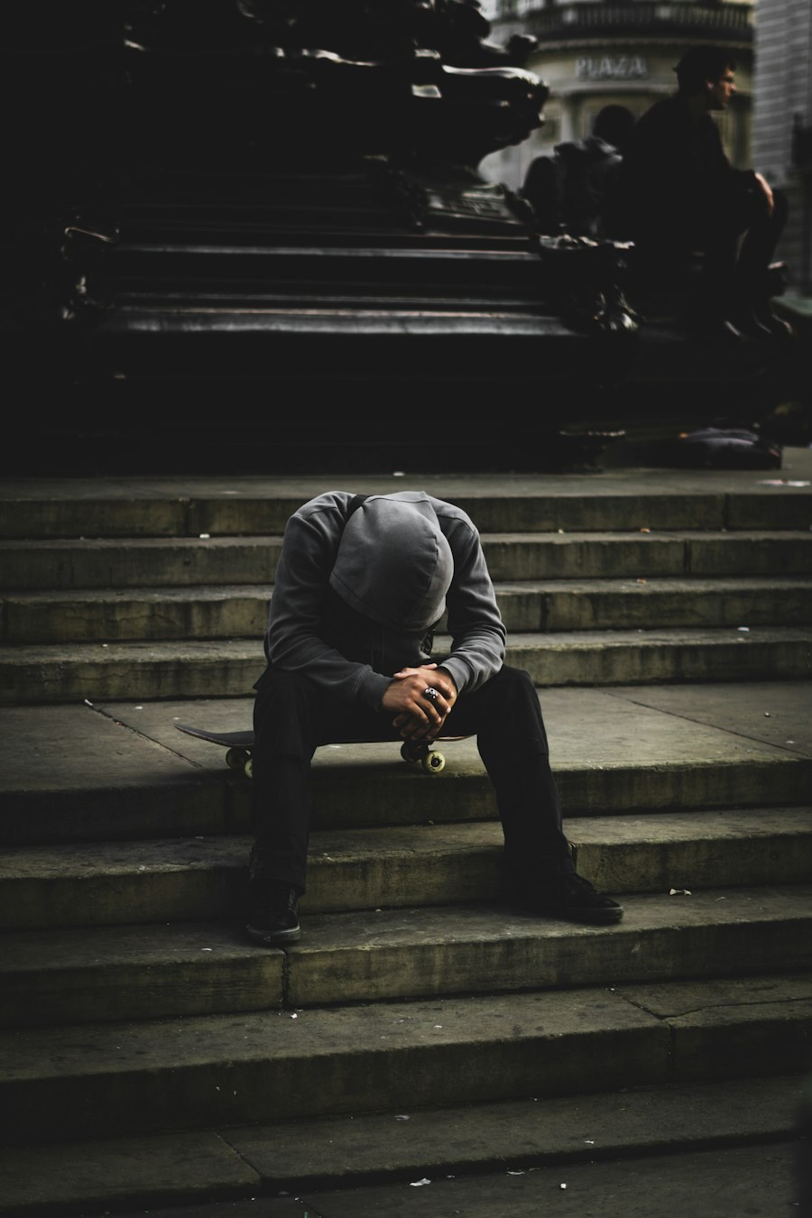 A person sitting alone on stone steps with their head in their hands.
